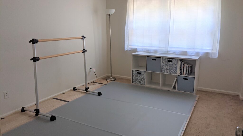 "After" picture of dance floor on carpet project - grey marley floor, white cube shelf unit, ballet barre, and a lamp in the corner