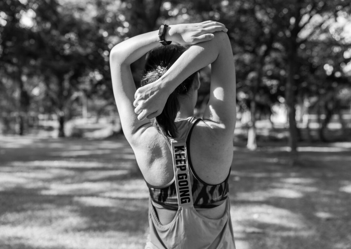 Woman doing an arm stretch in a park with her back to the camera | Dance Insight: Tips for Dancing in Extreme Heat