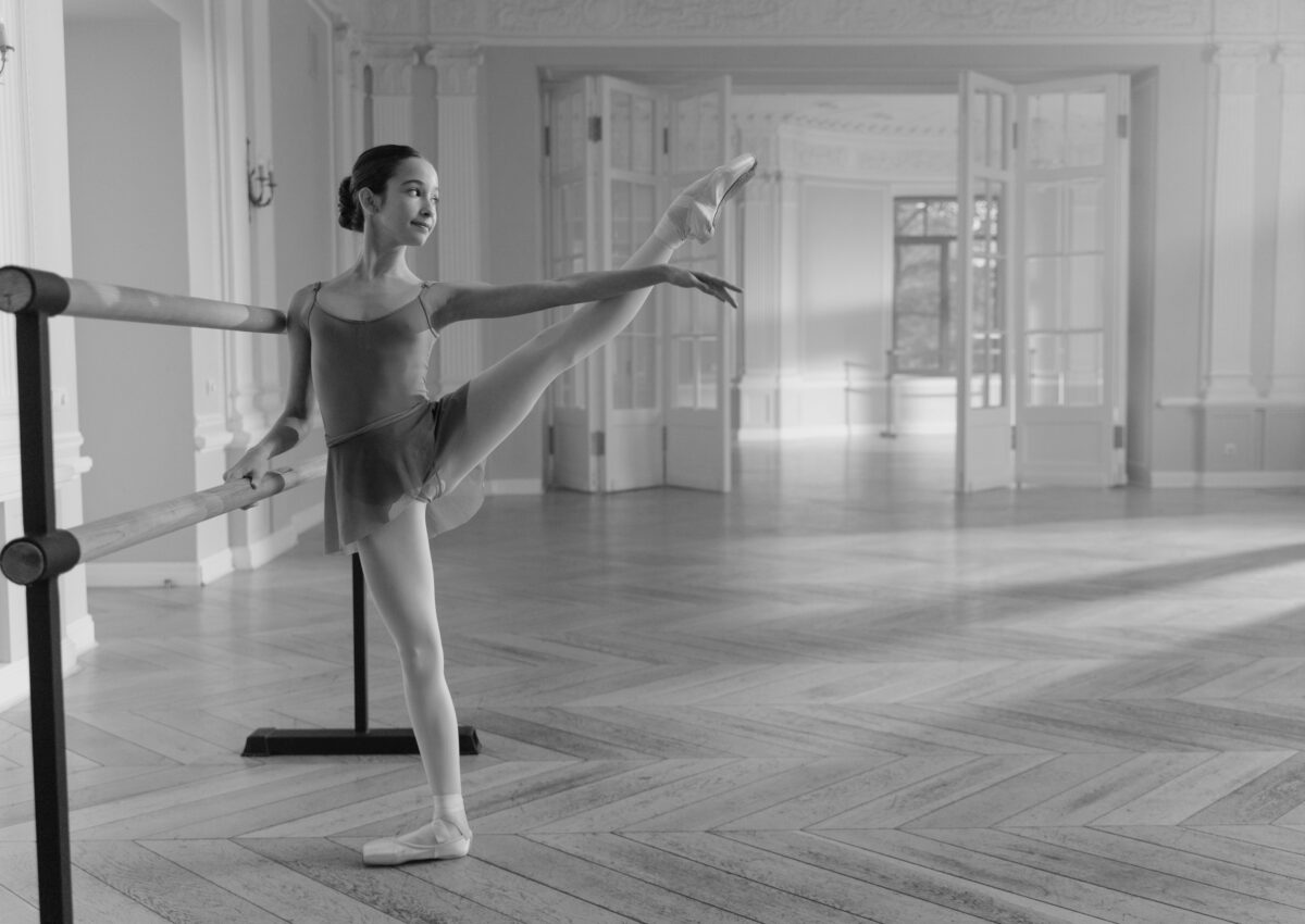 black and white photo of teen girl at a ballet barre with a leg extended to the side | workout for higher extensions