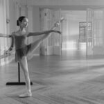 black and white photo of teen girl at a ballet barre with a leg extended to the side | workout for higher extensions