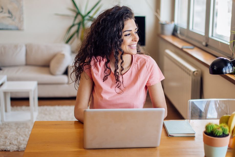 woman in pink shirt sits at desk with computer | side hustle ideas for dancers actors performers | Dance Insight