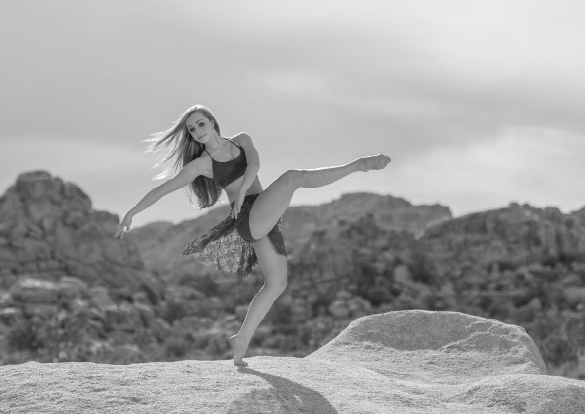 Black and white photo of a young woman dancing with mountains in the distance